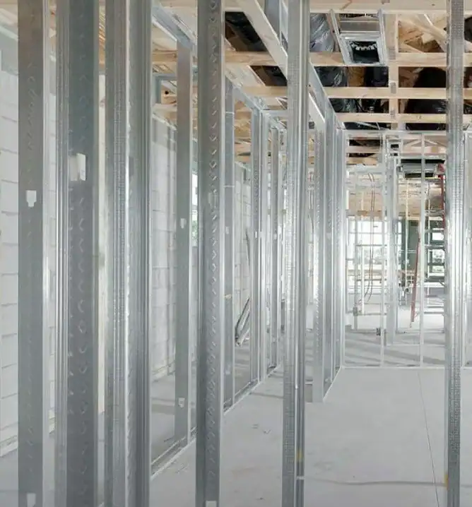 Montants et ossatures métalliques à l'intérieur d'un bâtiment en construction, avec des poutres de plafond apparentes et des murs non finis.